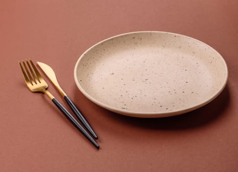 Empty ceramic plate on a monochrome brown background. Empty plate with cutlery on a dining table