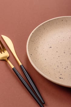 Empty ceramic plate on a monochrome brown background. Empty plate with cutlery on a dining table