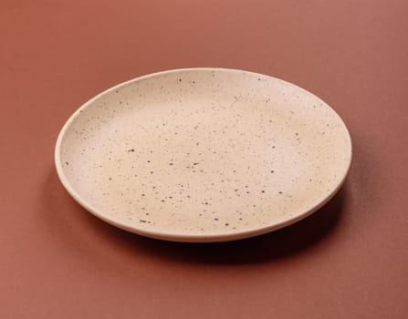 Empty ceramic plate on a monochrome brown background. Empty plate with cutlery on a dining table
