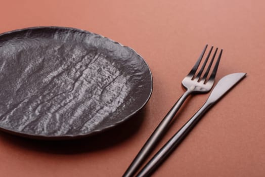 Empty ceramic plate on a monochrome brown background. Empty plate with cutlery on a dining table