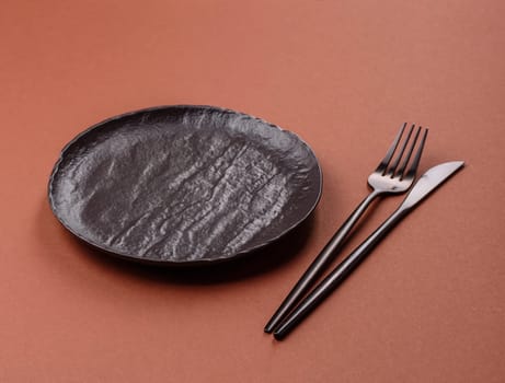 Empty ceramic plate on a monochrome brown background. Empty plate with cutlery on a dining table