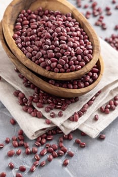 Wooden bowls full of dried red azuki beans on folded napkin on gray table closeup. Vegetarian protein source from legumes. Traditional East Asian cousin ingredient