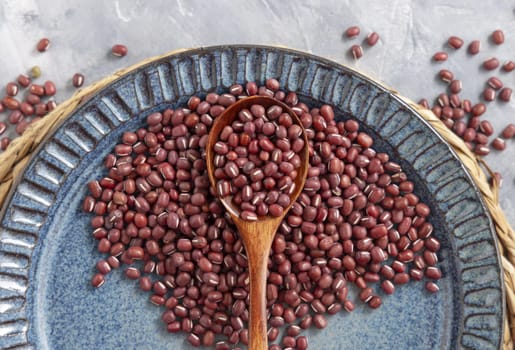 Ceramic blue plate full of dried red azuki beans with a wooden spoon on grey table top view, copy space. Healthy vegetarian food, legumes protein source. Traditional East Asian cousin ingredient