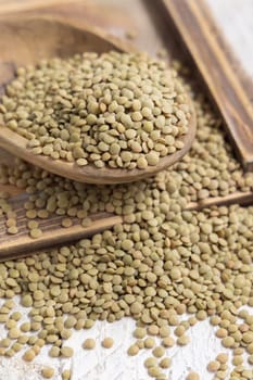 Wooden bowl full of dried raw green lentils on white table close up. Healthy raw vegetarian food, legumes plant-based protein source. Traditional mediterranean ingredient
