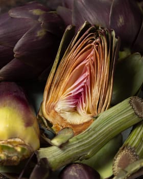 Cut purple raw artichokes on dark rustic table closeup. Fresh vegetables bought on farmers market ready to cook. Italian cousine ingredient