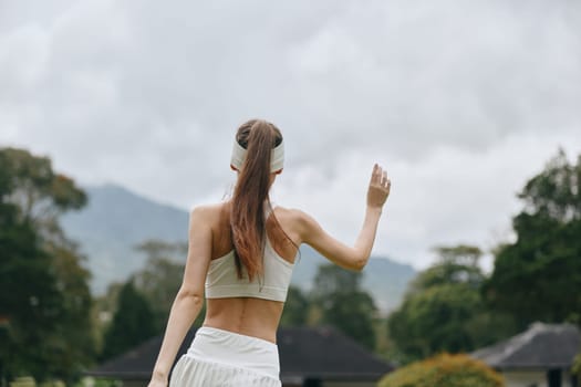 Active woman in white sportswear stands outdoors, promoting a healthy lifestyle and fitness Nature backdrop enhances sense of freedom and vitality