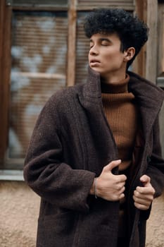 Fashion man in brown coat and turtle neck sweater standing in front of old building with window in background.