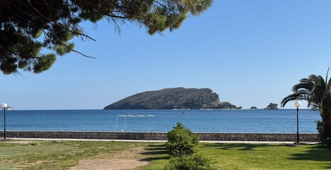 Scenic view of forested island surrounded by tranquil blue sea, framed by palm trees and coastal park. High quality photo