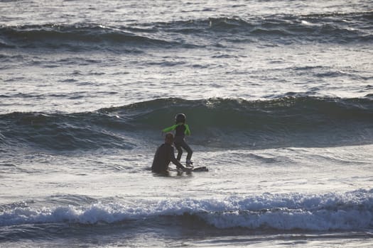 Surfing instructor father teaching a child how to surf, helping him balance on a surfboard in the ocean