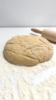 Fresh Dough on Floured Surface with Rolling Pin in a Kitchen Setting. Fresh dough resting on a floured surface with a rolling pin nearby, perfect for baking. Perfectly captures the simplicity and preparation stages of culinary creations in a home or bakery environment.