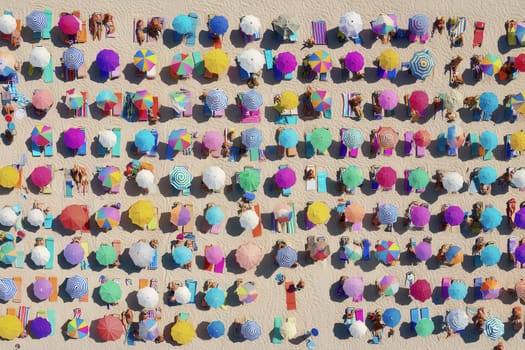 Colorful umbrellas and sunbathers arranged in rows on a sunny beach captured from above. Perfect for vacation ads, summer visuals, and lifestyle content