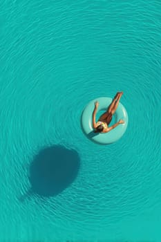 Minimalist aerial view of a woman on a float in a turquoise pool with sun reflections and gentle ripples. Great for wellness, summer visuals, luxury lifestyle, and vacation ads