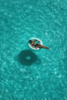 Young woman floats on a turquoise pool in the sun, enjoying a calm and relaxing summer moment. Perfect for wellness, holiday visuals, resort promotion, and lifestyle content