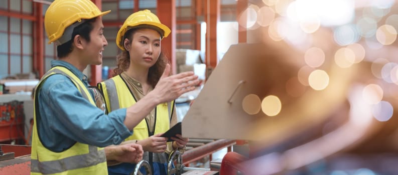 Industrial engineer man and worker operation woman training work on metal sheet ironing machine, two engineering wear safety helmet they talking together about machinery in factory manufacture