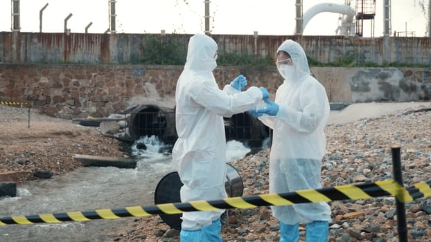 Ecologist sampling water from the river with test tube, Scientist or Biologist in a protective suit and protect mask collects sample of waste water from industrial for analyze, problem environment