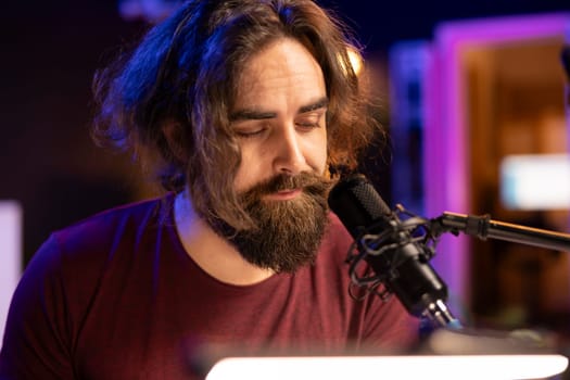Talented musician producer singing a new song on microphone in home studio, composing music an creating tunes with piano keyboard and daw software. Artist works with electronic equipment.