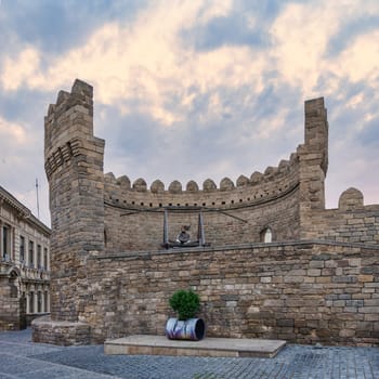 A trebuchet stands prominently at the walls of Icherisheher, the old city of Baku, Azerbaijan. The structure showcases historical weaponry against a backdrop of a dramatic sky at twilight