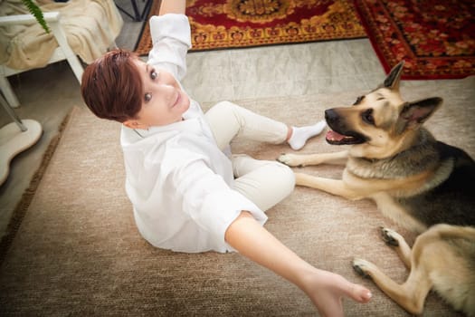 A middle-aged woman sits on the floor with her German Shepherd dog, enjoying a fun and relaxed moment together.