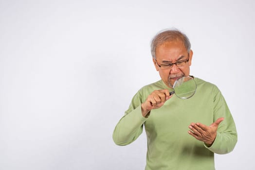 Portrait Asian old man with glasses is looking through a magnifying glass studio shot isolated on white background. senior man use magnifier zoom on hand