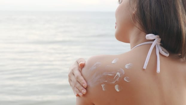 Beautiful Asian woman applying sun protection cream on tanned shoulder on the beach, sun Cream, Close up female in bikini using sunscreen lotion on back body before sunbathing