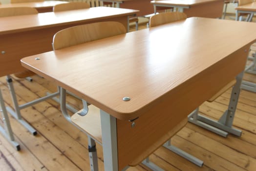 Wooden desks and chairs positioned in perfect rows on shiny wooden floor. Bright sunlight streams into well-organized classroom. Metal legs add sturdy and sleek design.For modern academic and learning