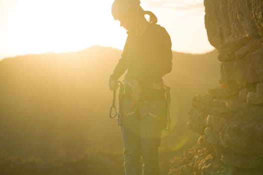 Young girl is preparing for training on the rocks sunset, in the mountains and puts a helmet on her head for safety to protect her health, woman engaged in active sports, in mountaineering and rock climbing.