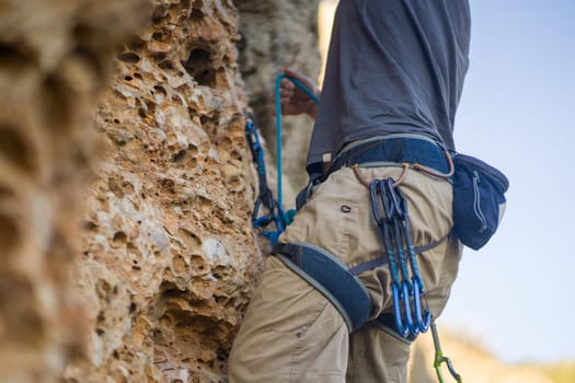 A young strong sporty man is engaged in rock climbing and mountaineering, a man's hand holds a climbing gear, a quickdraw close-up against a background of red rocks on a sunny day.