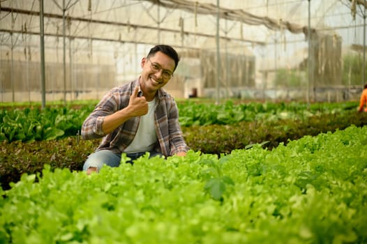 Smiling farmer giving a thumbs up gesture while inspecting plants in a greenhouse.