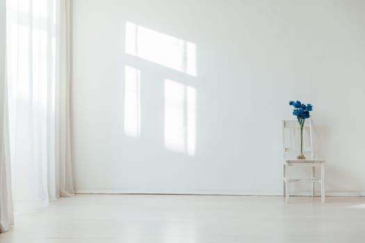 One vintage chair and vase with blue flowers in the interior of a white room with a window