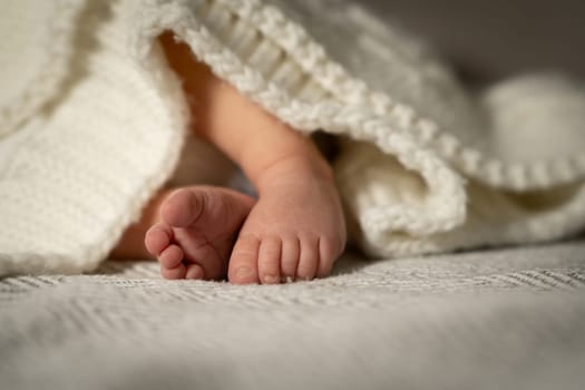 Soft baby feet emerge playfully from beneath a warm blanket in a tranquil nursery, capturing a moment of innocence and comfort during the afternoon.