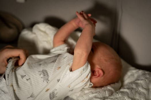 In a softly lit room, a mother lovingly plays with her infant, who raises their arms joyfully on a cozy blanket, showcasing their bond.
