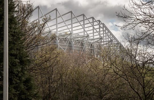 Newcastle, UK - Apr 13, 2025 - Looking through the bushes in a park at the steel structure of St James' Park stadium with the sky in the background. use it as your Wallpaper, Poster and Space for text, Selective focus.
