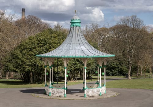 Newcastle, UK - Apr 13, 2025 - View of A Bandstand And A Grandstand. It’s a modern replica of the Victorian bandstand that had been installed in the Leazes park. The Music Pavilion with Green trees in the background, use it as your Wallpaper, Poster and Space for text, Selective focus.