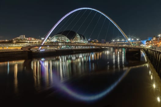 Newcastle, UK - Apr 13, 2025 - Night view of The Iconic gateshead millennium bridge spanning the River Tyne with Sage Gateshead with Tyne Bridge in the background. The pedestrian bridge with reflection in river, use it as your Wallpaper, Poster and Space for text, Selective focus.