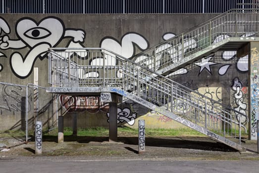 Newcastle, UK - Apr 13, 2025 - A staircase with Street art graffiti walls by the River tyne. Silver steel stairs descend from textured walls toward graffiti decorated lower levels, use it as your Wallpaper, Poster and Space for text, Selective focus.