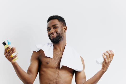 Shirtless man with lotion bottle and towel, showcasing daily skincare routine and personal grooming essentials.