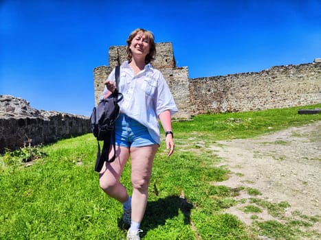 A woman walks through vibrant green grass near ancient stone ruins, enjoying a sunny day of exploration and adventure outdoors.