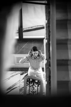 A woman stands at a staircase in St. Petersburg, carefully adjusting her hair and preparing herself for an outing in the daylight.