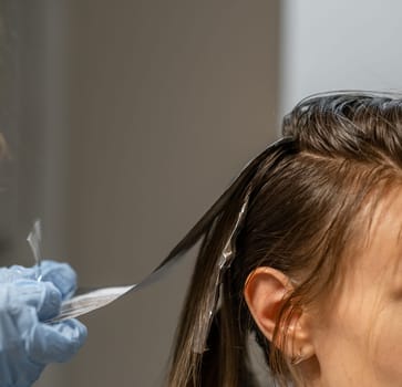 A stylist is carefully applying foil highlights to a clients hair during a hair coloring session in a modern salon setting.