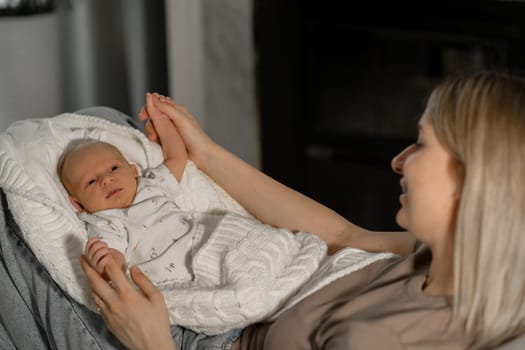 A mother lovingly interacts with her baby, cradling the child in a blanket while sitting comfortably indoors, creating a warm atmosphere.