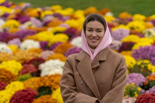 A woman wearing a pink headscarf stands happily among vibrant flowers in a beautiful garden during spring.