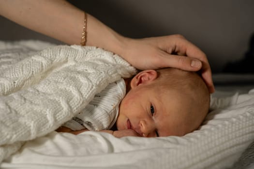 A mother gently caresses her sleeping newborn, wrapped warmly in a soft blanket in a serene and cozy environment during the evening.