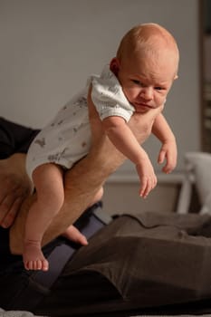 A small baby is being held in a playful manner by an adults arm indoors. The setting feels warm and inviting, capturing a joyful interaction.