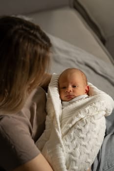 A mother lovingly cradles her newborn swaddled in a soft blanket, creating a tender connection in a serene indoor environment during morning light