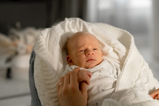 A mother cradles her infant in her arms while they sit together in a serene indoor setting. The soft sunlight creates a warm atmosphere.