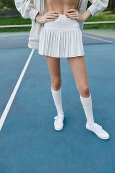 Confident young woman wearing a white pleated skirt and knee high socks, posing on a tennis court, embodying an energetic and athletic vibe perfect for sports themed content