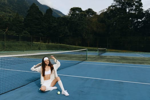 Energetic young woman in white activewear, excitedly sitting on a tennis court, exuding confidence and joy, set against a vibrant green background, perfect for sports related projects