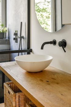 A serene bathroom featuring a stylish wooden countertop, a modern bowl sink, and large windows providing natural light, enhancing the minimalist design.
