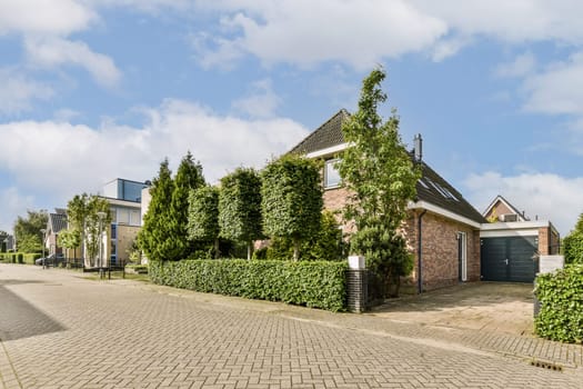 A serene residential area showcases modern architecture complemented by well-maintained landscaping, including lush trees and hedges, under a bright sky.