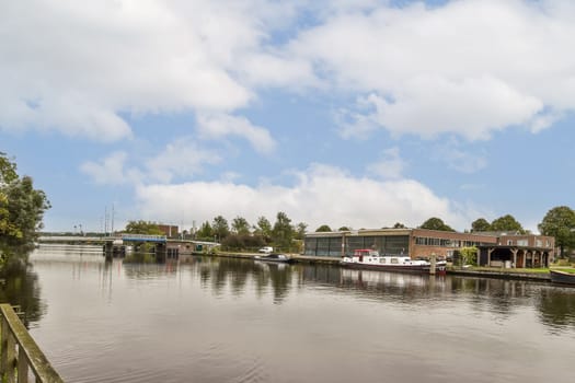 A picturesque waterside scene showcasing boats moored along a serene riverbank, surrounded by lush greenery and beautiful cloud formations.
